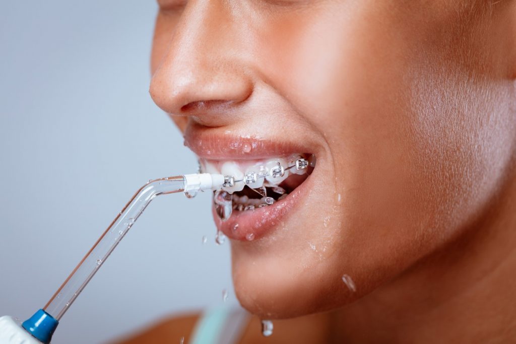 Person using water pick to clean around braces