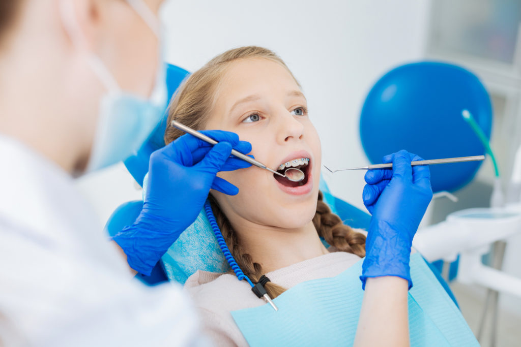 Regular checkup. Pleasant blonde young girl lying on a dental chair and opening her mouth while having a regular checkup