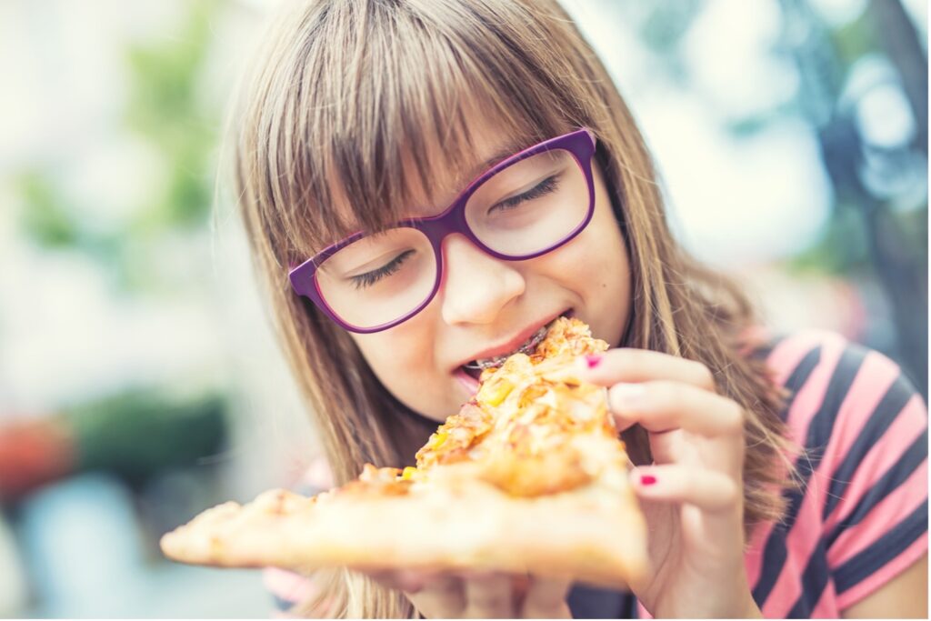 A young person with braces eating a slice of pizza, How Sugar Affects Your Braces