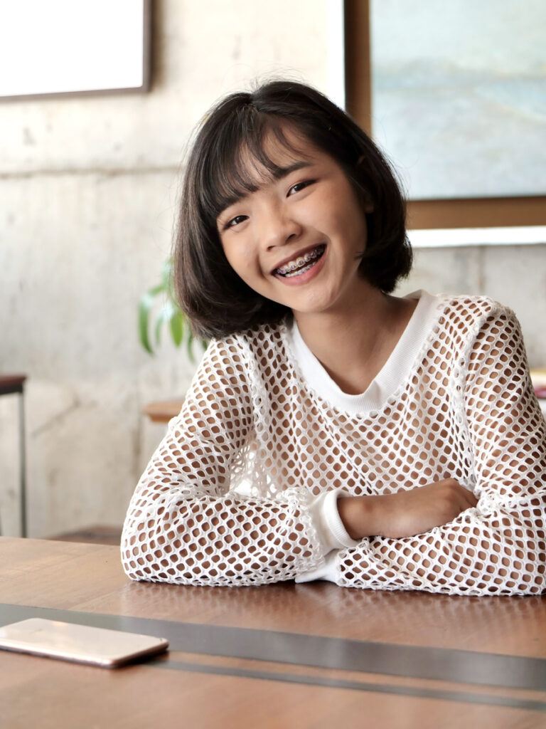 young person sitting a desk smiling, Unlocking Smiles: Exploring the Power of Dentofacial Orthopedics at McDonough Orthodontics
