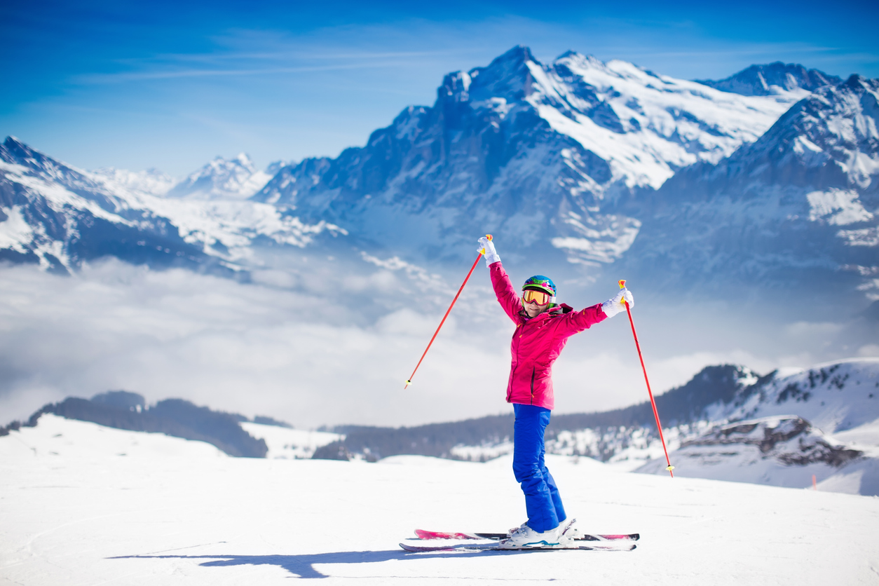 Winter Sports and Braces: Protecting Your Smile on the Slopes and Ice, Young active woman skiing in mountains. Female skier kid with safety helmet, goggles and poles enjoying sunny winter day in Swiss Alps. Ski race for adults. Winter and snow sport in alpine resort.