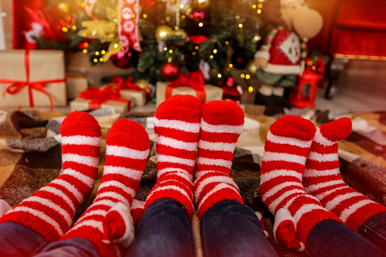 The 12 Days of Braces: Holiday Braces Tips from McDonough Orthodontics, Warm socks in red and white stripes on the background of the Christmas tree