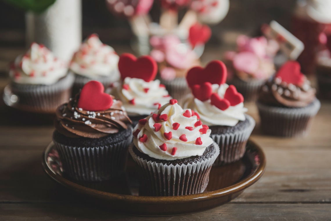 Chocolate cupcakes topped with white and chocolate frosting, decorated with red heart sprinkles and heart-shaped toppers, representing sugary treats that can be problematic for braces.