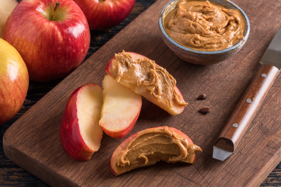 Sliced red apples spread with peanut butter on a wooden cutting board, showing a sticky food combination that can be difficult to clean from braces.