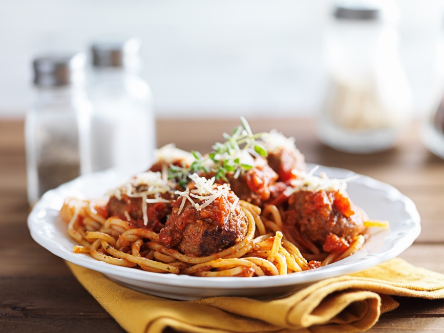 Plate of spaghetti and meatballs topped with tomato sauce and grated cheese, representing a softer meal option that is generally easier to eat with braces.