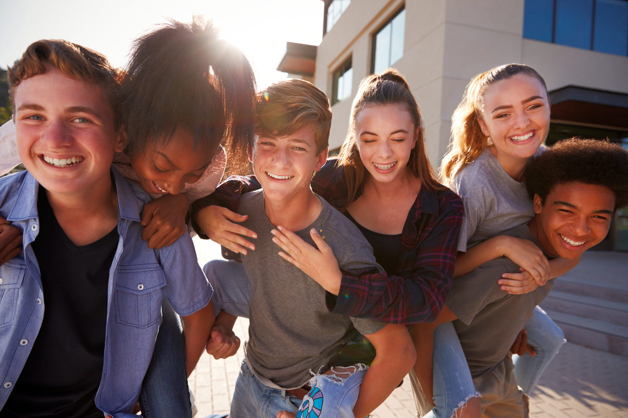 Smiling group of teens hanging out outdoors, including some wearing braces, reflecting the confidence supported by teen orthodontic care at McDonough Orthodontics.