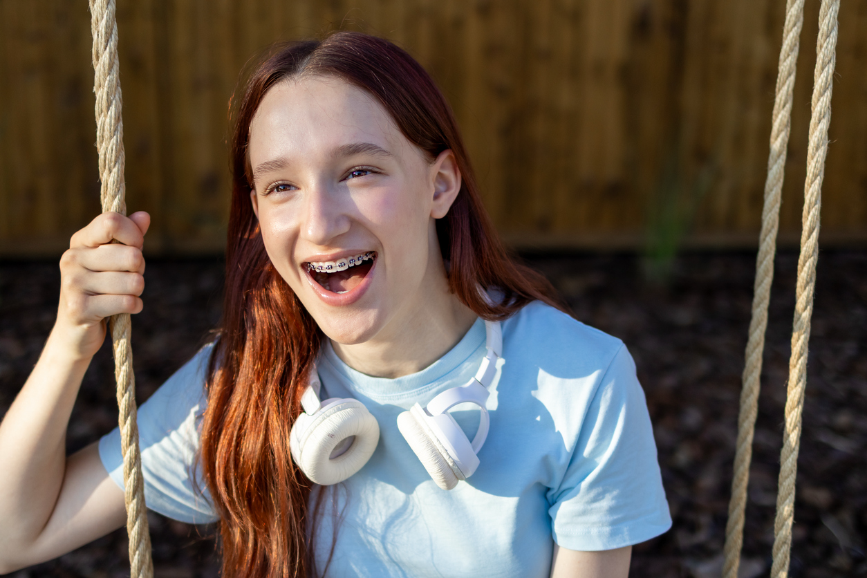 Teen girl smiling with braces while sitting on a swing.
